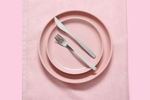 Pink dinner plates with silver fork and knife on a pink tablecloth, minimalis Stock Photos