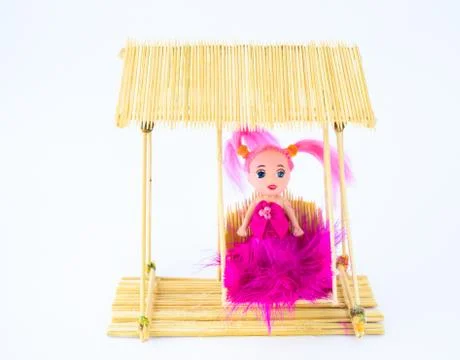 A pink doll sitting on a wooden swing made of toothpicks with an isolated whi Stock Photos