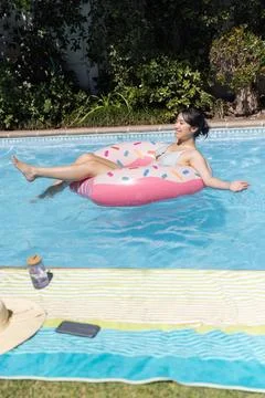 Pink donut pool float drifting on backyard pool water, displaying towel, hat, Stock Photos