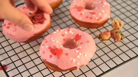 Pink doughnuts on the baking rack. Valentine's Day concept. Woman hand Stock Footage 145122246