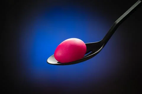 Pink Easter egg in a spoon in the center of the bright blue spots on a black  Stock Photos