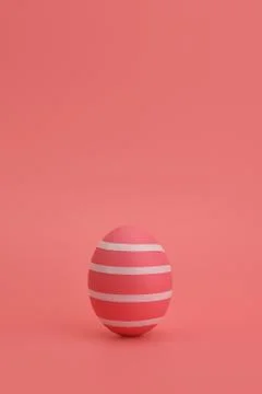 Pink Easter egg with white stripes stands against pink background. Stock Photos