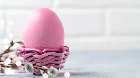 Pink Easter egg in a wicker stand on a gray table with pussy-willow twigs - E Stock Photos
