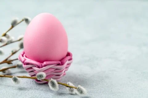 Pink Easter egg in a wicker stand on a gray table with pussy-willow twigs - E Stock Photos