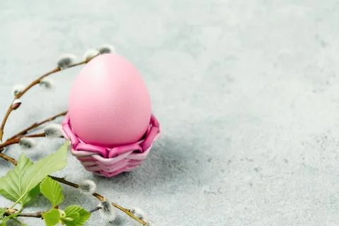 Pink Easter egg in a wicker stand on a gray table with pussy-willow twigs - E Stock Photos