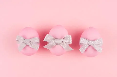 Pink easter eggs with grey bows in row on pastel pink background, top view. Stock Photos