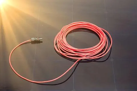 Pink electrical wire coiled on dark surface with sunlight Stock Photos