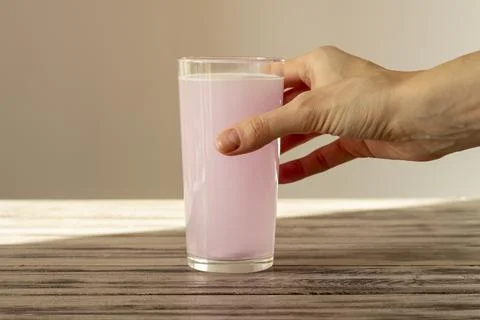 The pink electrolyte tablet dissolves in water. The woman's hand holds a glass Foto stock