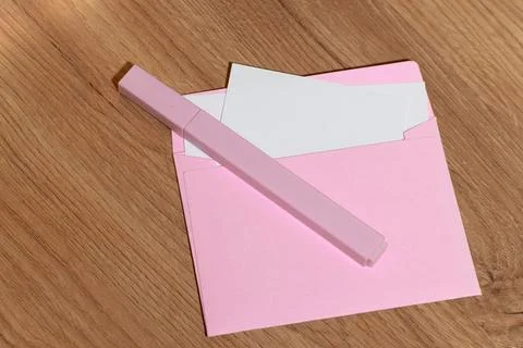 Pink envelope with white insert and pink pen on wooden table Stock Photos