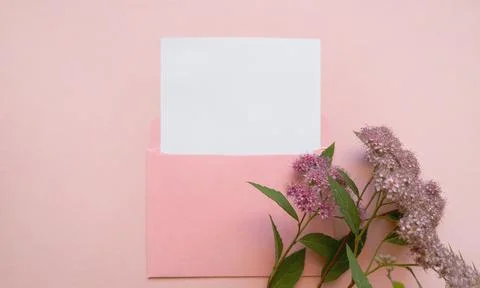 Pink envelope with a white mockup sheet and pink flowers next to it on pink Stock Photos
