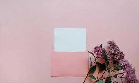 Pink envelope with a white mockup sheet and pink flowers next to it on pink Stock Photos