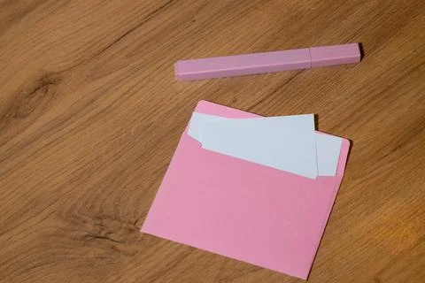 A pink envelope with white paper inside sits on a wooden table next to a pink Stock Photos