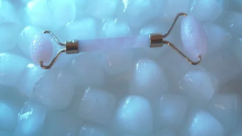Pink face roller scraping for aesthetic facial massage on ice cubes and water Stock Footage 314852907