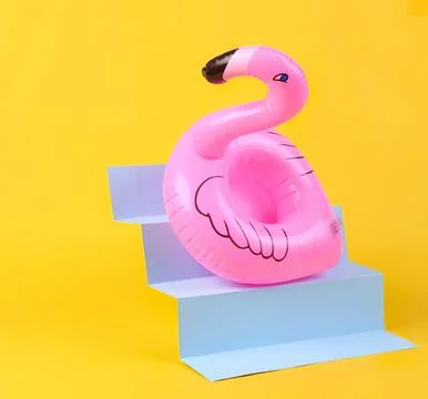 Pink flamingo pool float sitting on blue steps with yellow background Stock Photos