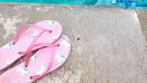 Pink flip-flops on the concrete by the pool on a sunny summer day Stock Footage 308772539