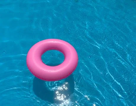 Pink float ring in clear swimming pool water on a sunny day Stock Photos