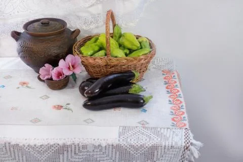 Pink flowers, eggplants, bell peppers, and a clay pot with a lid. Stock Photos