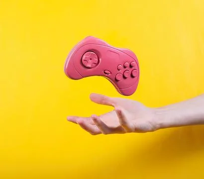 Pink game controller floating above hand against yellow background Stock Photos