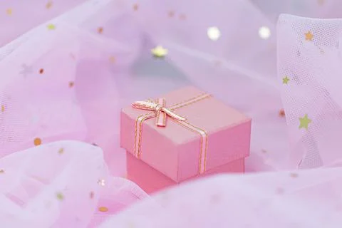 Pink gift box with golden bow lies on sparkling background. Gift wrapping for Stock Photos