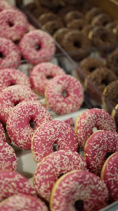 Pink glazed donuts with white sprinkles and chocolate donuts in bakery display Stock Footage 345356559