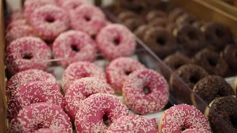 Pink glazed donuts with white sprinkles displayed beside chocolate donuts Stock Footage 345358166