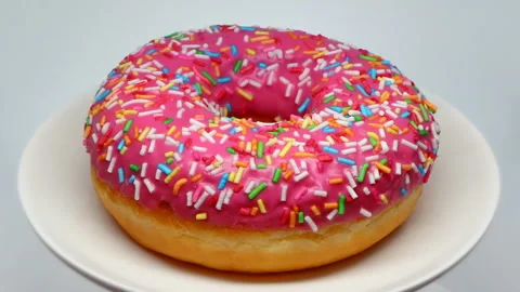 Pink glazed doughnut on plate rotating macro Video stock 143489892