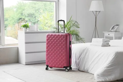 Pink hard shell suitcase with geometric pattern standing in a bright hotel ro Stock Photos
