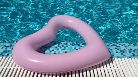 Pink heart-shaped inflatable ring bobbing on sparkling turquoise water Stock Footage 311662288