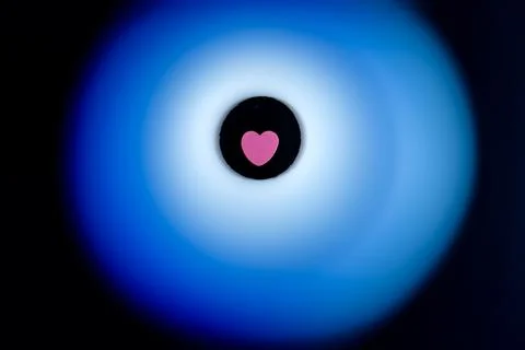 Pink heart surrounded by soft blue glow on black background. Stock Photos