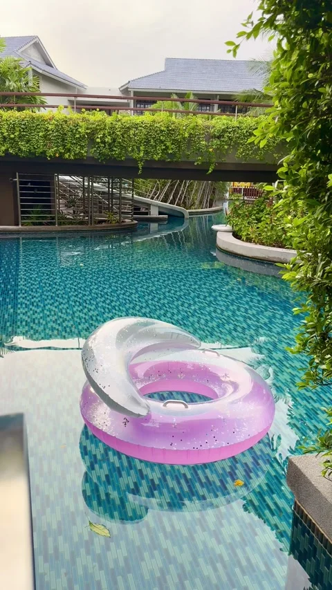 Pink inflatable chair peacefully floating across a luxury resort pool with Vídeos de archivo 345888686