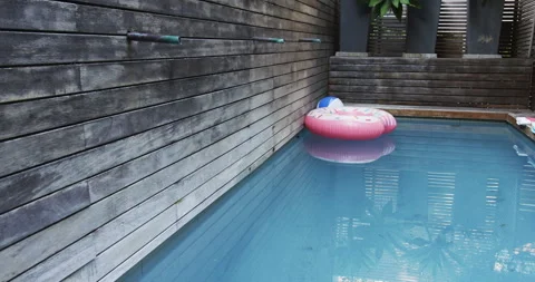 Pink inflatable donut float drifting in backyard pool, with beach ball and Stock Footage 316122278