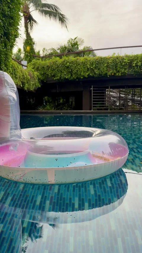Pink inflatable lounger floating on blue pool water, surrounded by palm trees Vídeos de archivo 345888660