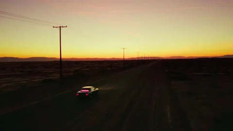 Pink interior car driving down lone desert road as drone follows Stock Footage 221993687