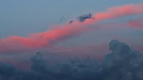 Pink light on elongated cloud formation across sky with dark cumuliform clouds Stock Footage 344095092