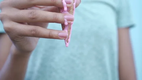 Pink melting ice cream flows down in slow motion on the fingers of a black girl Stock Footage 94493489