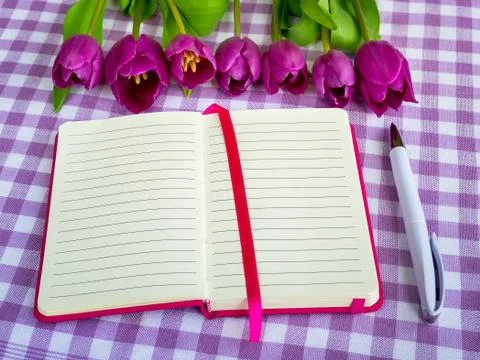 Pink notepad with lined paper, white ballpoint pen and a row of purple tulips Stock Photos