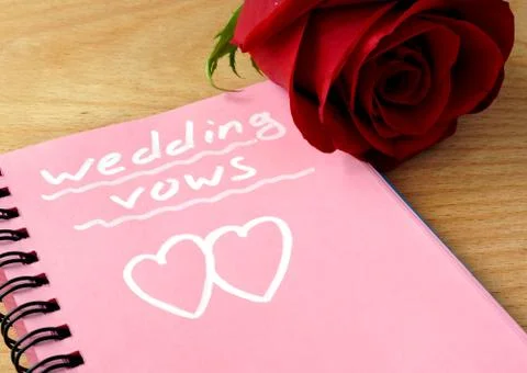 Pink notepad with wedding vows and rose on a wooden background. Stock Photos