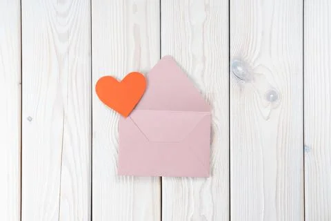 Pink opened envelope on white wooden background. Red cardboard heart is taken Stock Photos