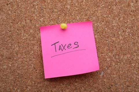 Pink paper note with phrase Taxes pinned to cork board, closeup Stock Photos
