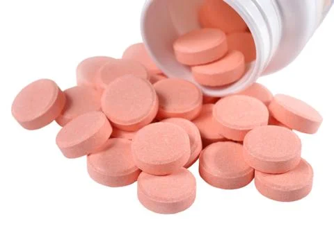 Pink pills spill out from bottle on a white Stock Photos