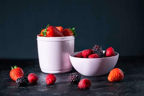 Pink plastic containers full of red fruits on a black background. Vegan food. Stock Photos