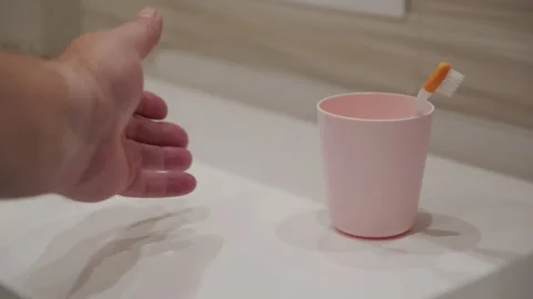 Pink Plastic Cup with Toothbrush Slides on Glossy White Bathroom Counter Stock Footage 321436563