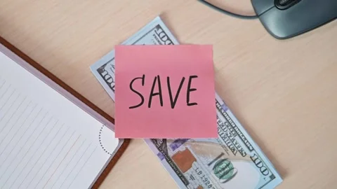 A pink post-it note marked with the word save is placed on a stack of cash on a Stock Footage 339094217