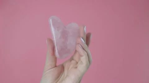 Pink quart gua sha in a woman's hand on a blue background, a copy of the space Stock Footage 132174778
