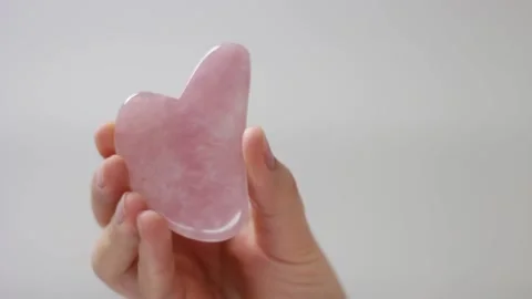 Pink quart gua sha in woman's hand on white background Stock Footage 137487621