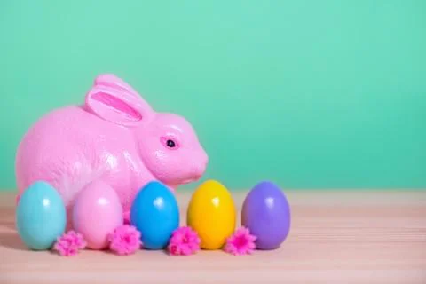Pink rabbit, row multi colored painted Easter eggs and flowers over green bac Stock Photos