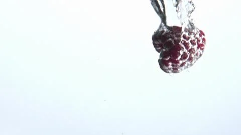 Pink raspberry fall splashed water goblet closeup. Sparkling clear aqua berries Stock Photos