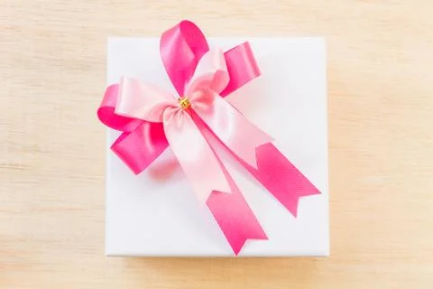 Pink ribbon bow and white gift box on wooden background. Stock Photos