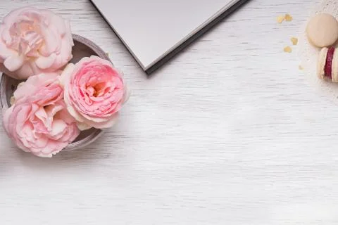 Pink roses, notepad, clock and macarons on white wooden table Stock Photos