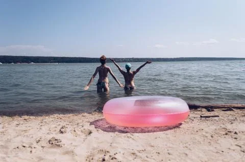 Pink rubber pool ring lying on sand and happy friends enjoing summertime stan Stock Photos